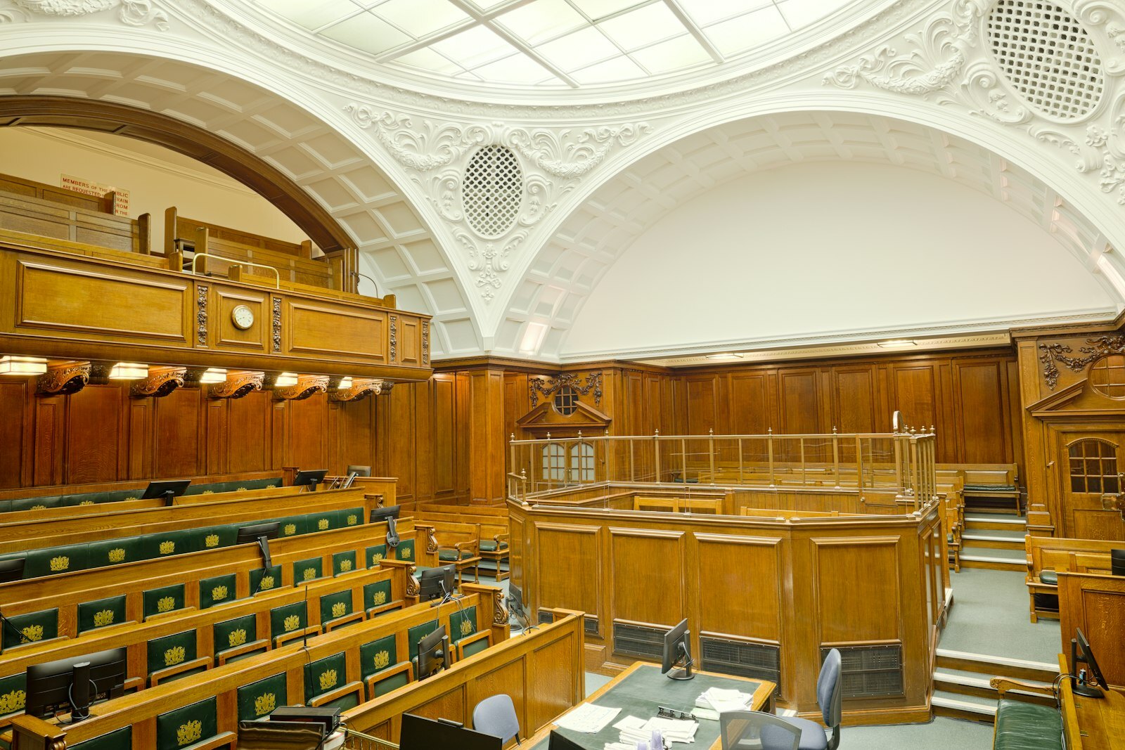 Empty ornate courtroom interior with wooden paneling and green seats
