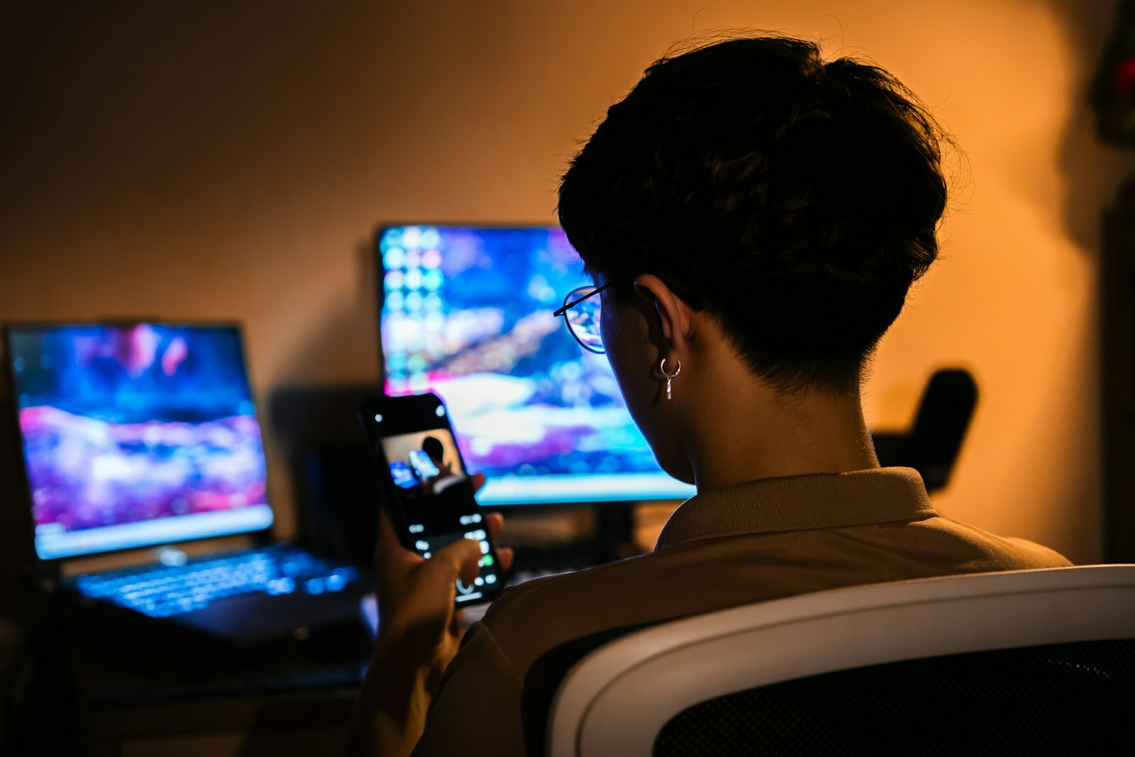 Person uses smartphone with glowing computer screens in dark room